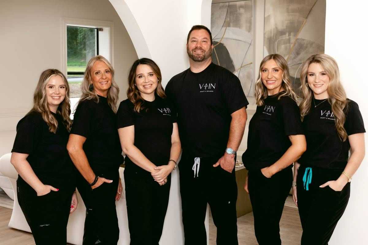 Group of six smiling people in matching VHN shirts inside a modern room.